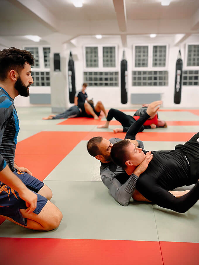 Trainer zeigt zwei anderen Männern eine Übung im BJJ Unterrciht im Combat Club Cologne